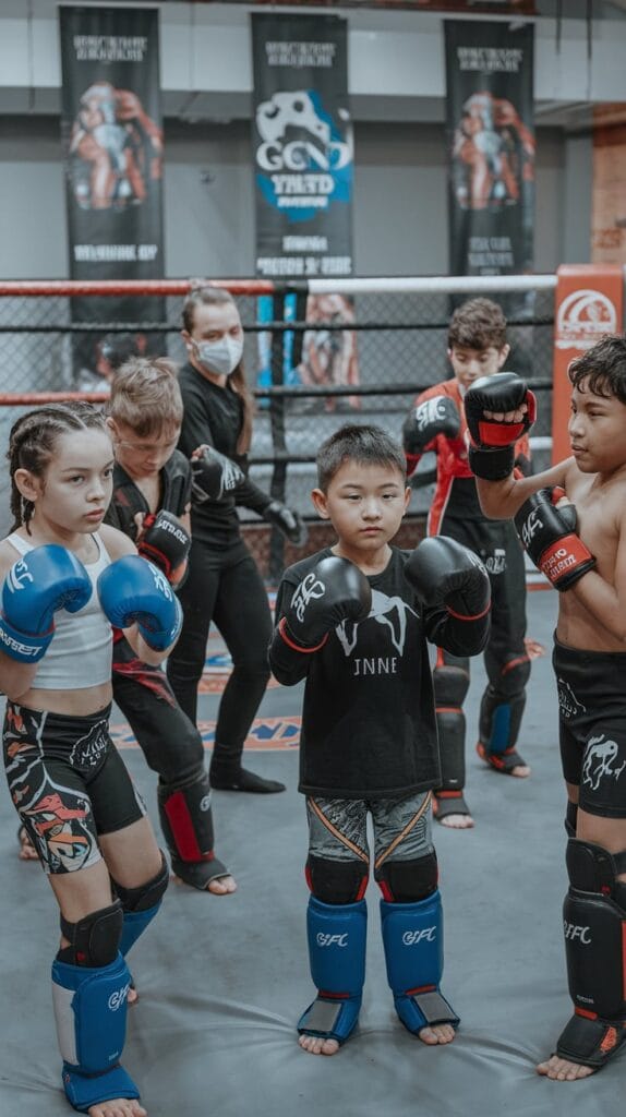 A group of young MMA fighters in protective gear preparing for a youth MMA tournament, emphasizing teamwork and skill-building